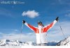 smiling_man_holding_ski_poles_with_arms_outstretched_on_snowy_mountain_31634.jpg