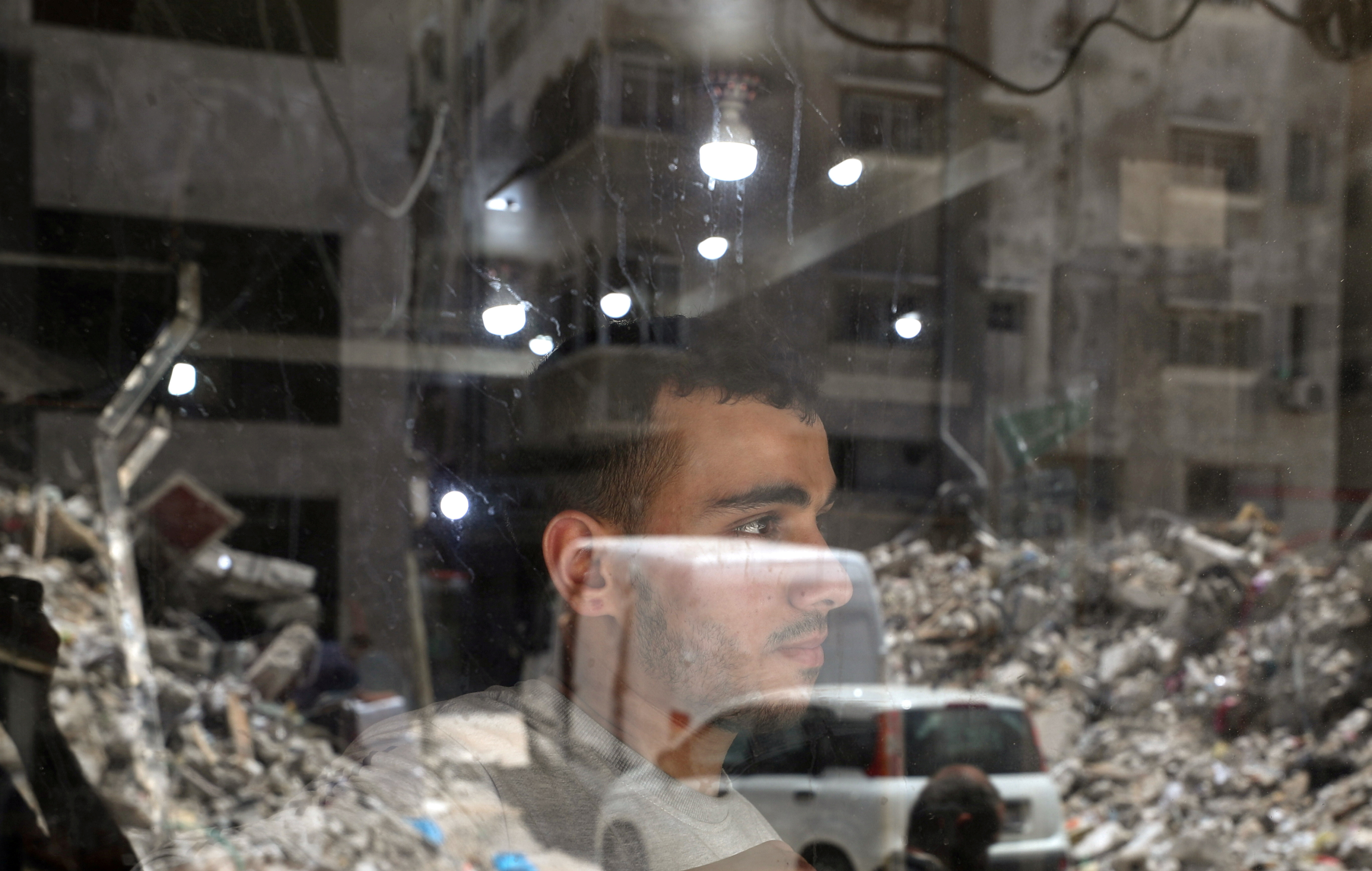 A Palestinian man looks out as the remains of a building, which was destroyed in Israeli air strikes, are reflected in a window, amid Israeli-Palestinian fighting, in Gaza, May 20, 2021. REUTERS/Mohammed Salem     TPX IMAGES OF THE DAY